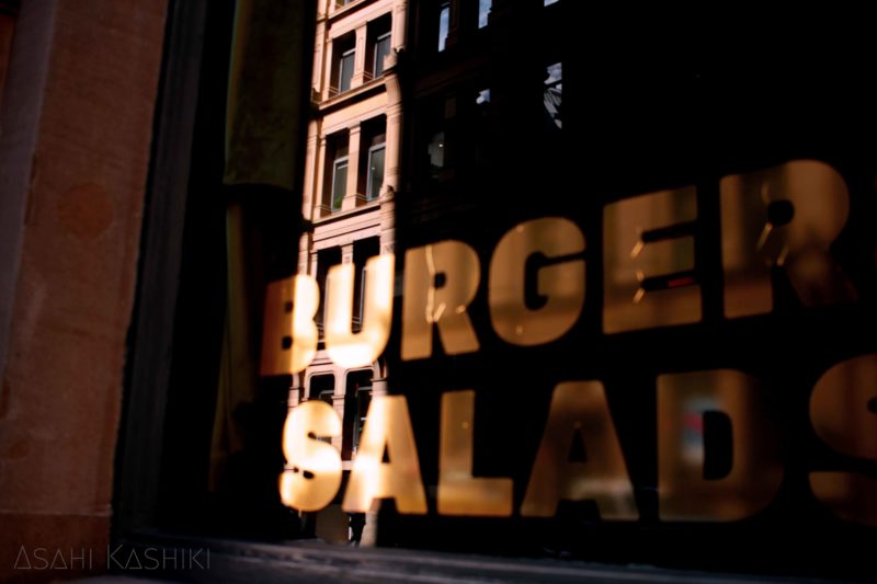 the window reflecting the front building, on that glass the words "burgers, salads" are written with gold letters.
