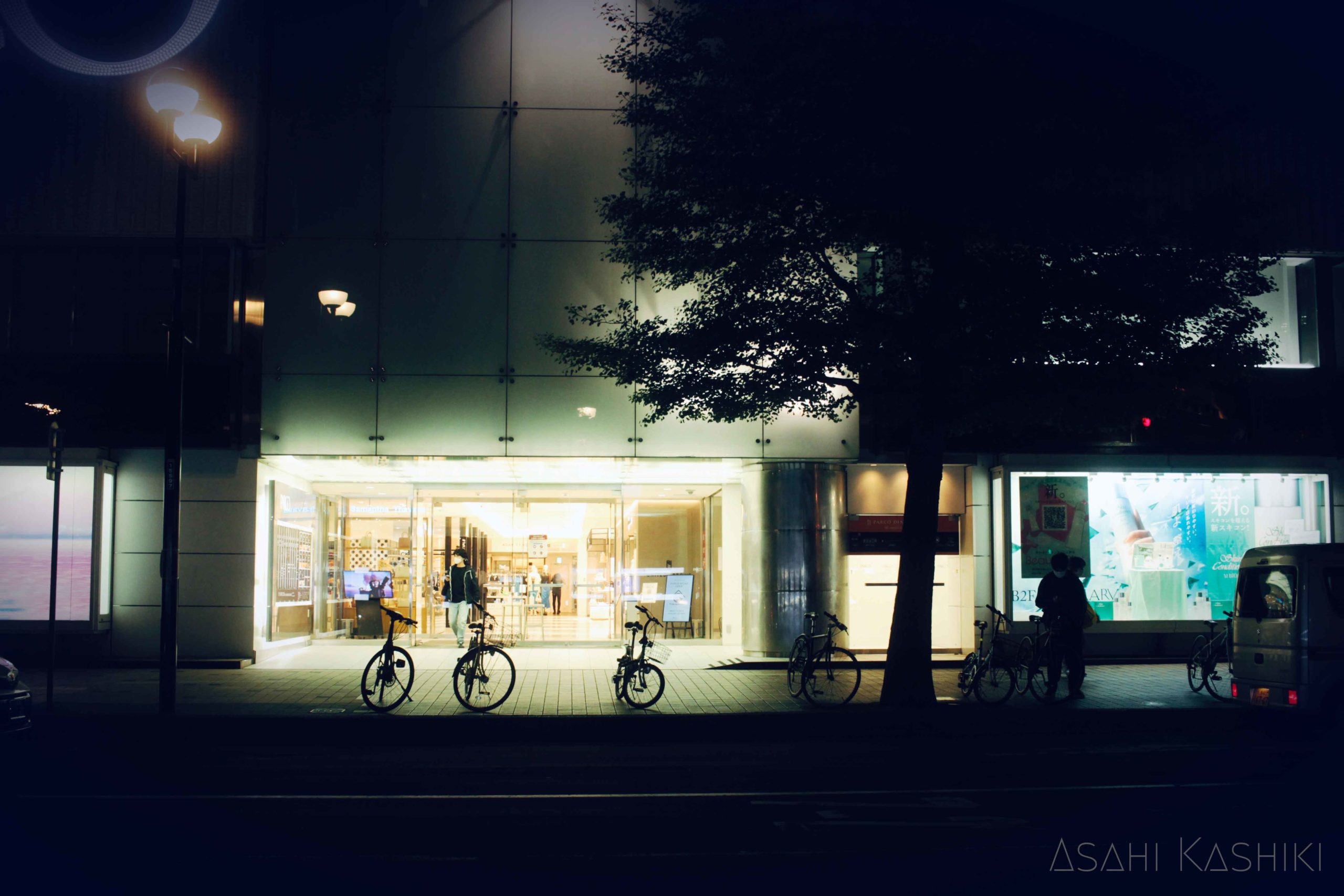 閉店間際のデパートから出てくる人の影と、その前に並ぶ自転車