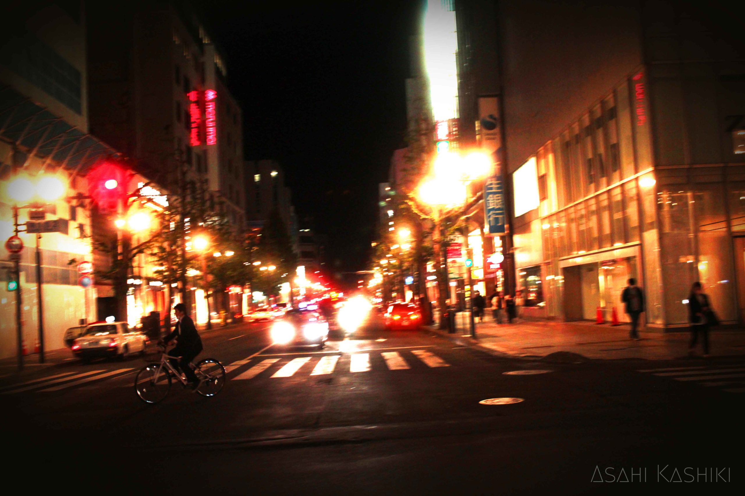夜の通りの写真。街灯や車の明かりが明るく光る